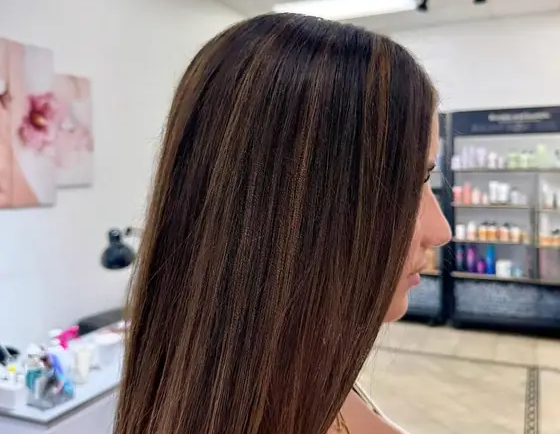 Side profile of a woman with long straight brown hair and subtle highlights in a hair salon.